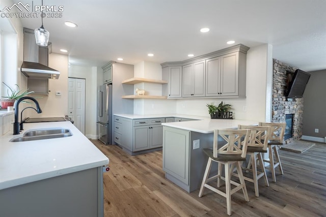 kitchen with wall chimney exhaust hood, a peninsula, gray cabinets, open shelves, and a sink