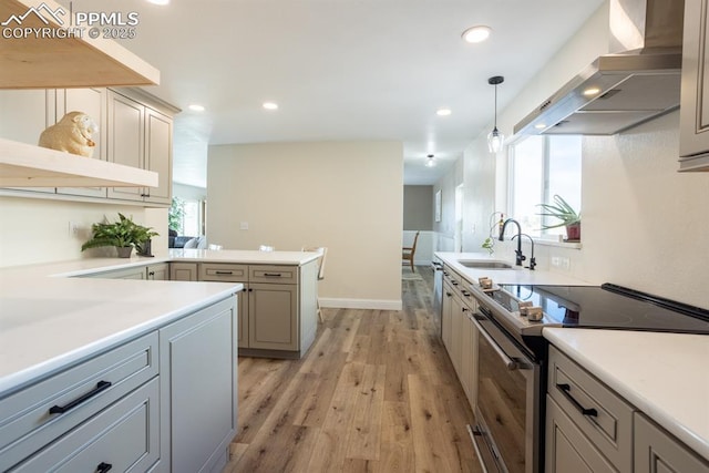 kitchen with a peninsula, electric range, a sink, wall chimney range hood, and light wood finished floors