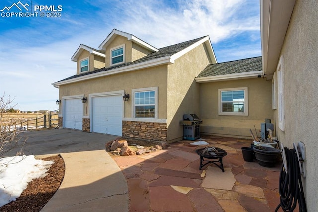 exterior space featuring stone siding, an outdoor fire pit, fence, and stucco siding