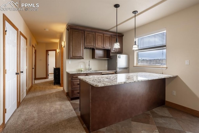 kitchen featuring a peninsula, a sink, baseboards, freestanding refrigerator, and decorative light fixtures