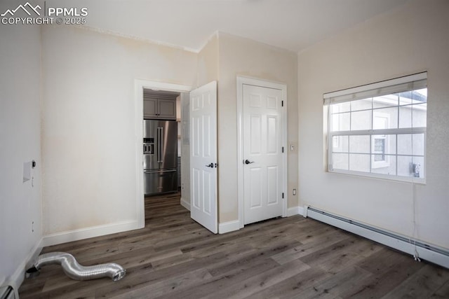 unfurnished bedroom with high end fridge, a baseboard radiator, wood finished floors, and baseboards