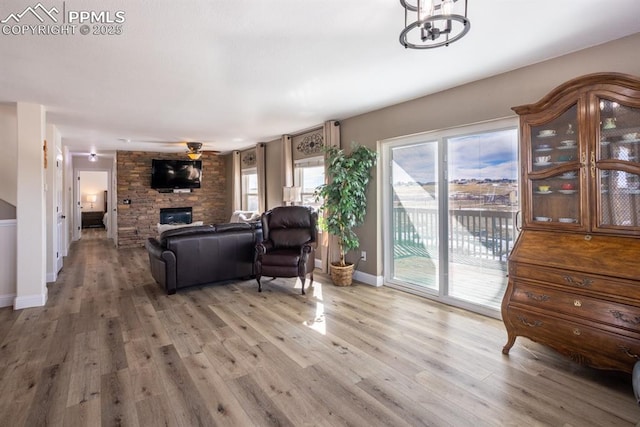 living room featuring light wood-type flooring, a healthy amount of sunlight, a stone fireplace, and ceiling fan with notable chandelier