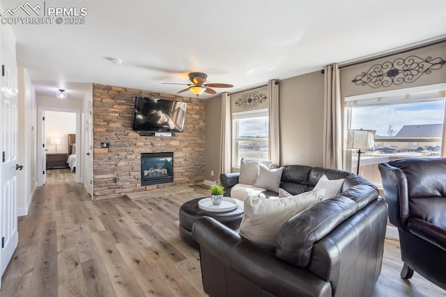 living area with light wood finished floors, ceiling fan, baseboards, and a stone fireplace