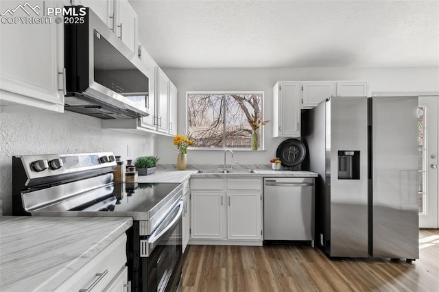 kitchen with stainless steel appliances, white cabinets, a sink, light stone countertops, and light wood-type flooring