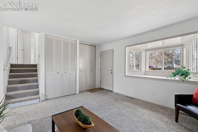 carpeted living room with a textured ceiling and stairway