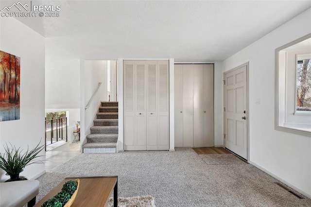 living area with a wealth of natural light, visible vents, stairway, and carpet flooring