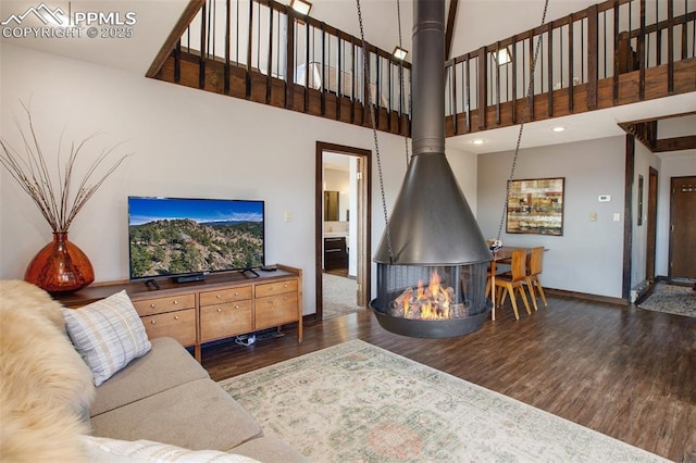 living room featuring baseboards, a towering ceiling, wood finished floors, a wood stove, and recessed lighting