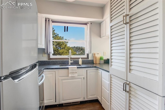 kitchen featuring freestanding refrigerator, white cabinets, a sink, and dark countertops