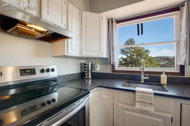 kitchen with dark countertops, electric range, white cabinets, a sink, and under cabinet range hood