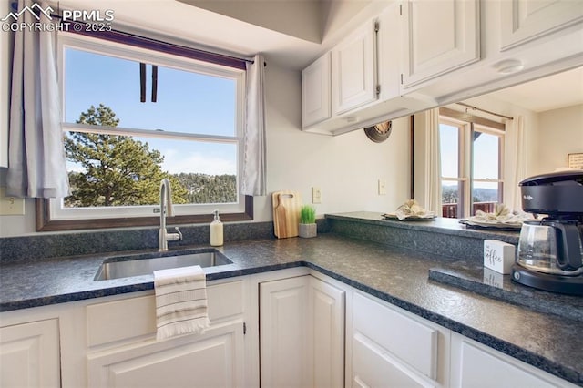 kitchen with a wealth of natural light, dark countertops, white cabinets, and a sink