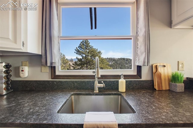 kitchen featuring white cabinetry, a sink, and dark stone countertops