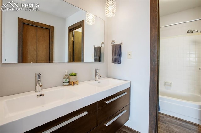 bathroom with double vanity, shower / bathtub combination, a sink, and wood finished floors