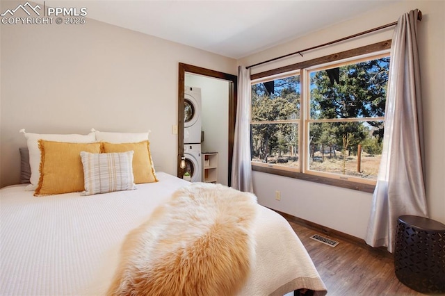 bedroom with baseboards, visible vents, stacked washing maching and dryer, and wood finished floors