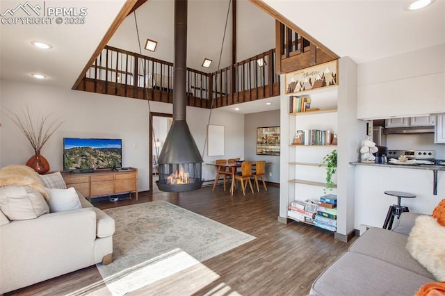 living room with recessed lighting, a high ceiling, wood finished floors, baseboards, and a wood stove