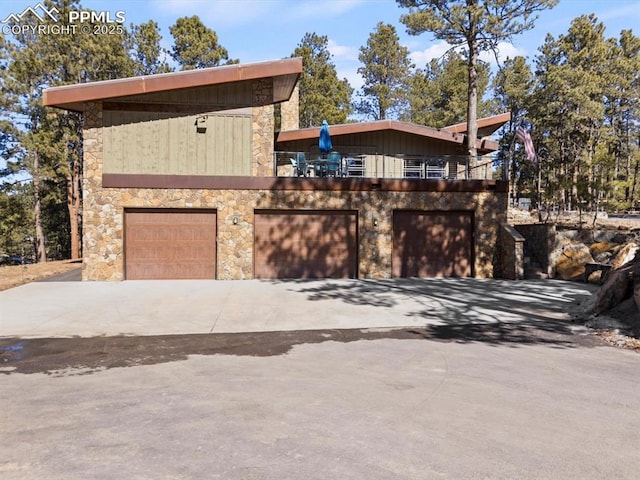 view of front of property featuring an attached garage, a balcony, driveway, and stone siding