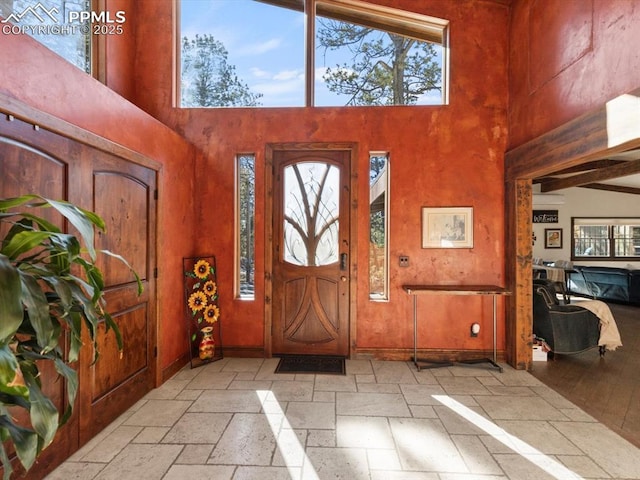 foyer entrance with a towering ceiling, stone tile flooring, and baseboards