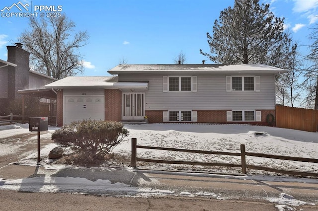 split level home with an attached garage, driveway, fence, and brick siding