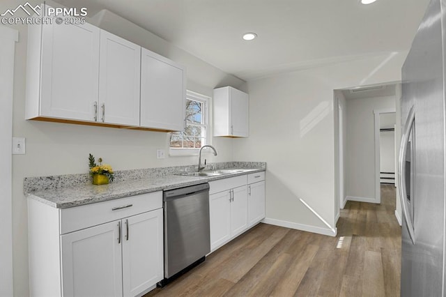 kitchen with light wood finished floors, appliances with stainless steel finishes, white cabinets, a sink, and baseboards