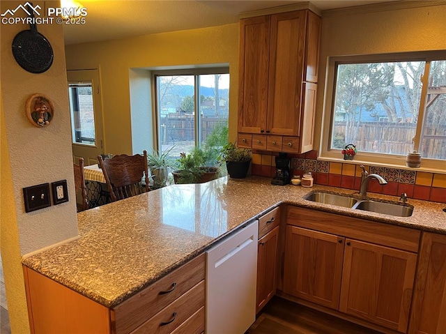 kitchen with light stone countertops, white dishwasher, brown cabinets, and a sink