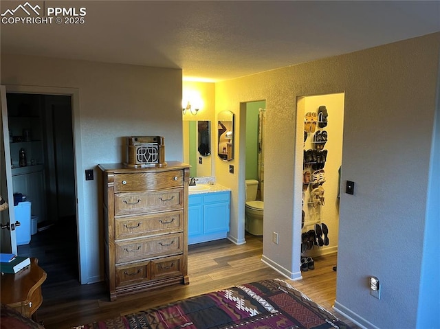 bedroom featuring light wood finished floors, a textured wall, ensuite bathroom, a walk in closet, and a sink