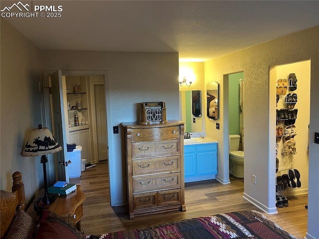 bedroom with light wood-style floors, a textured wall, a sink, and ensuite bathroom