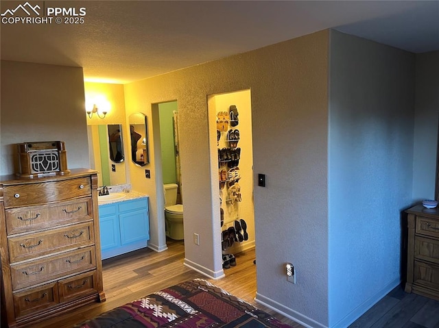 bedroom featuring light wood-style floors, connected bathroom, a sink, and a textured wall