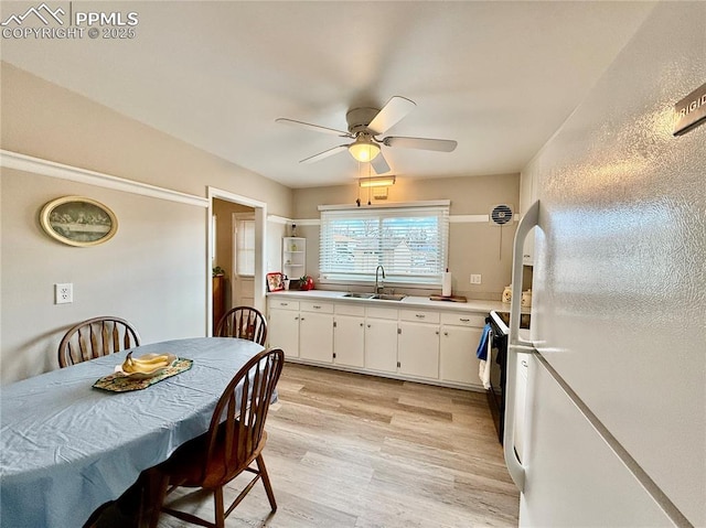 kitchen featuring white cabinets, freestanding refrigerator, light countertops, light wood-style floors, and a sink