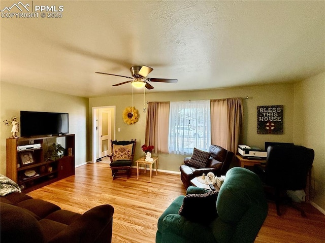 living room featuring a ceiling fan, a textured ceiling, baseboards, and wood finished floors