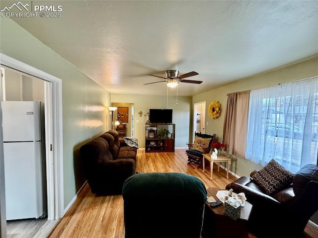 living area featuring light wood-style floors, a textured ceiling, baseboards, and a ceiling fan