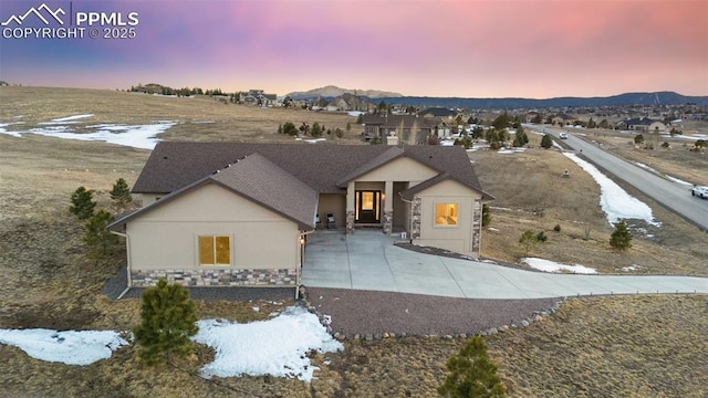 view of front of house featuring stone siding, roof with shingles, a mountain view, and stucco siding