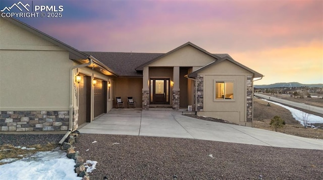 view of front of house with stone siding, an attached garage, driveway, and stucco siding