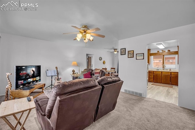 living room with a ceiling fan, visible vents, and light colored carpet