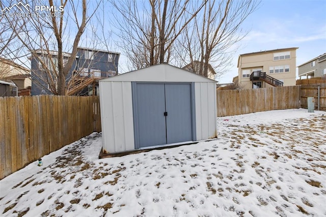 snow covered structure featuring a storage shed, a fenced backyard, and an outdoor structure