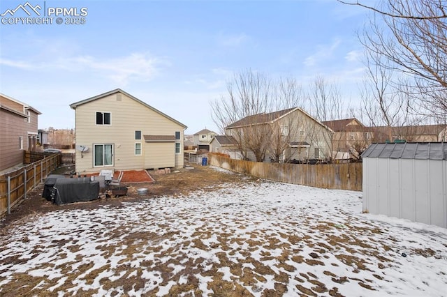 snow covered rear of property featuring a fenced backyard, a storage unit, and an outdoor structure