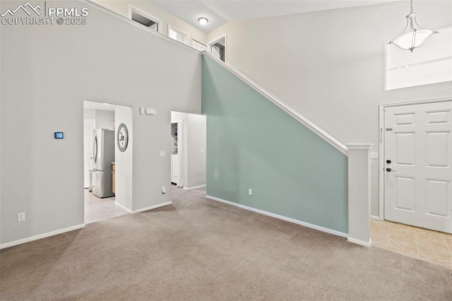 unfurnished living room featuring carpet, a high ceiling, and baseboards