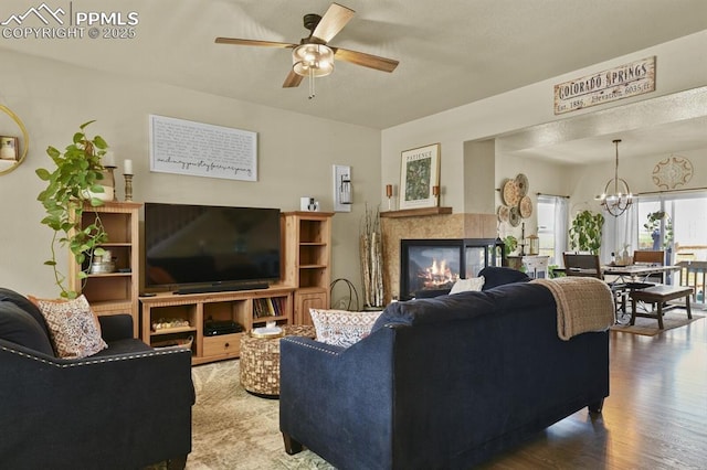 living room with a tiled fireplace, wood finished floors, and ceiling fan with notable chandelier