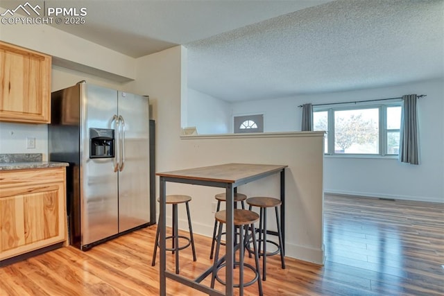 kitchen featuring a textured ceiling, light wood-style floors, baseboards, stainless steel fridge with ice dispenser, and light brown cabinetry