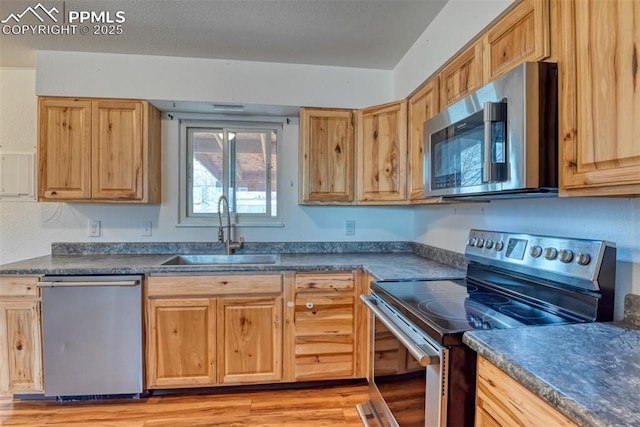 kitchen with dark countertops, light wood finished floors, appliances with stainless steel finishes, and a sink