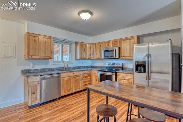 kitchen featuring dark countertops, light wood-type flooring, appliances with stainless steel finishes, and a sink