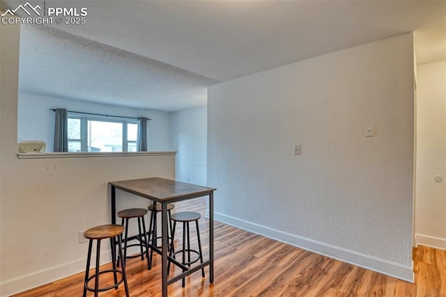 dining room with a textured ceiling, wood finished floors, and baseboards