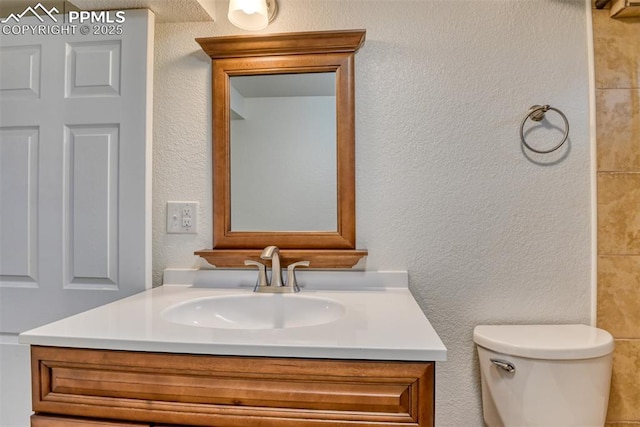 bathroom featuring a textured wall, vanity, and toilet