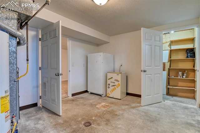 unfinished basement featuring a textured ceiling, freestanding refrigerator, and baseboards