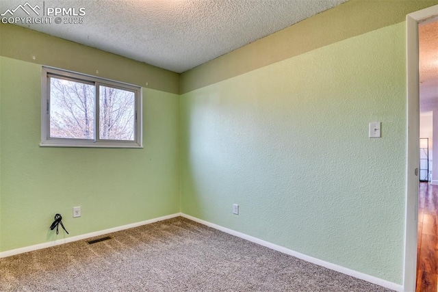 carpeted empty room featuring a textured ceiling, a textured wall, visible vents, and baseboards