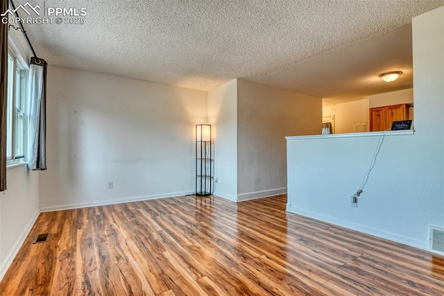 spare room featuring a textured ceiling, wood finished floors, visible vents, and baseboards