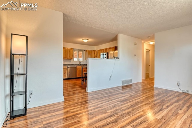 unfurnished living room featuring a textured ceiling, a sink, visible vents, baseboards, and light wood-type flooring