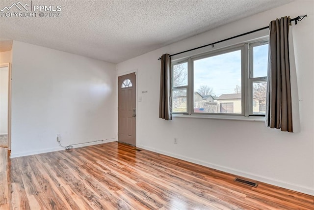 interior space featuring a textured ceiling, light wood finished floors, visible vents, and baseboards