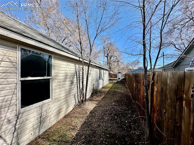 view of side of home featuring a shingled roof, fence, and an outdoor structure