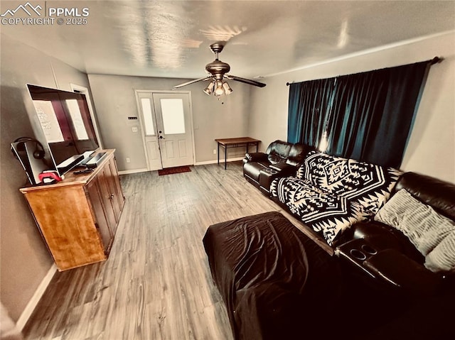 living area featuring wood finished floors, a ceiling fan, and baseboards