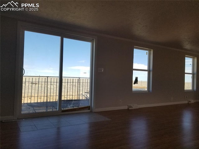 spare room with plenty of natural light, wood finished floors, visible vents, and crown molding