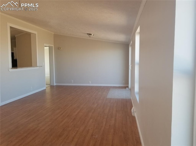 empty room with crown molding, a textured ceiling, baseboards, and wood finished floors